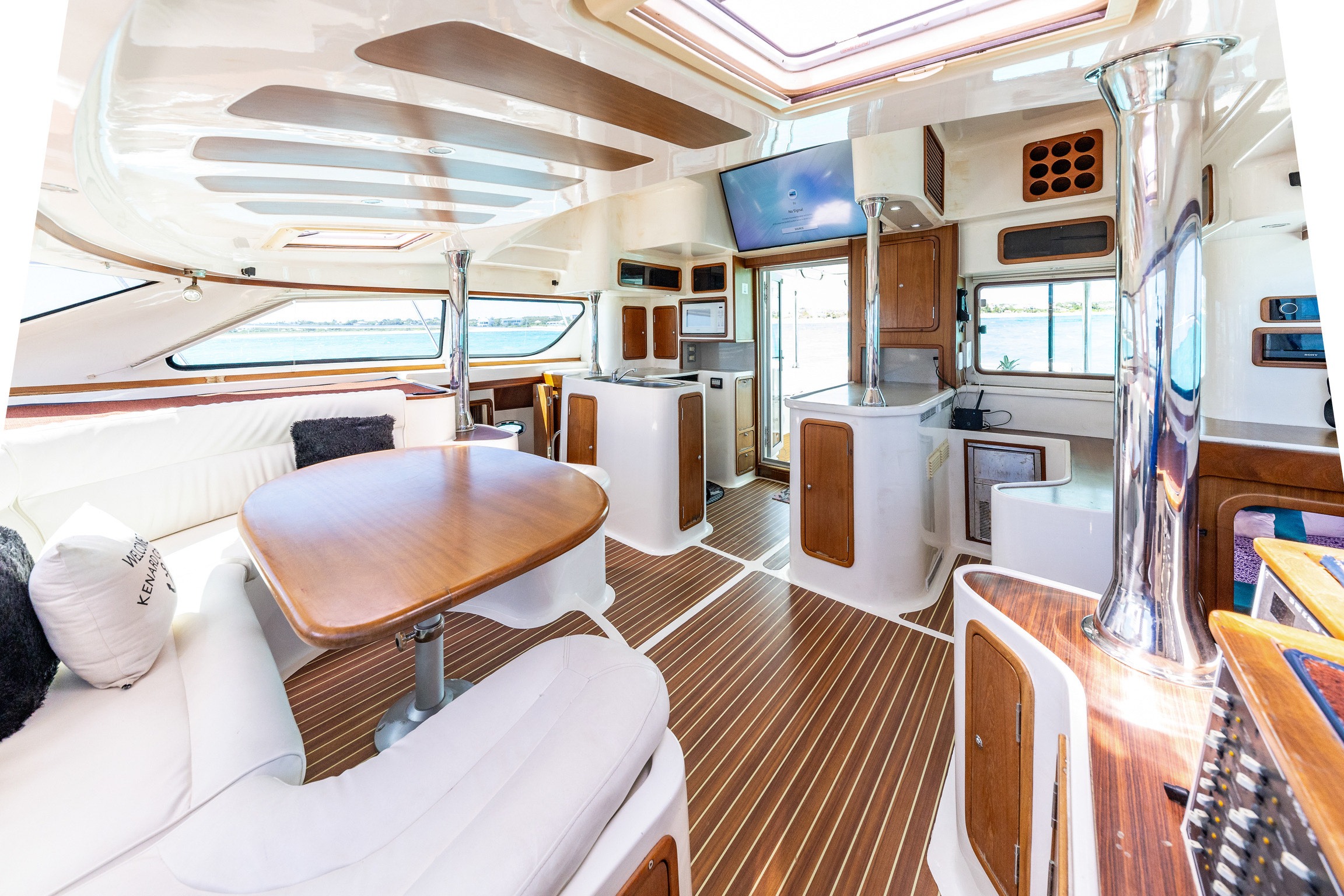 Modern yacht interior featuring a spacious seating area, a wooden dining table, and kitchen setup with large windows for natural light and water views.