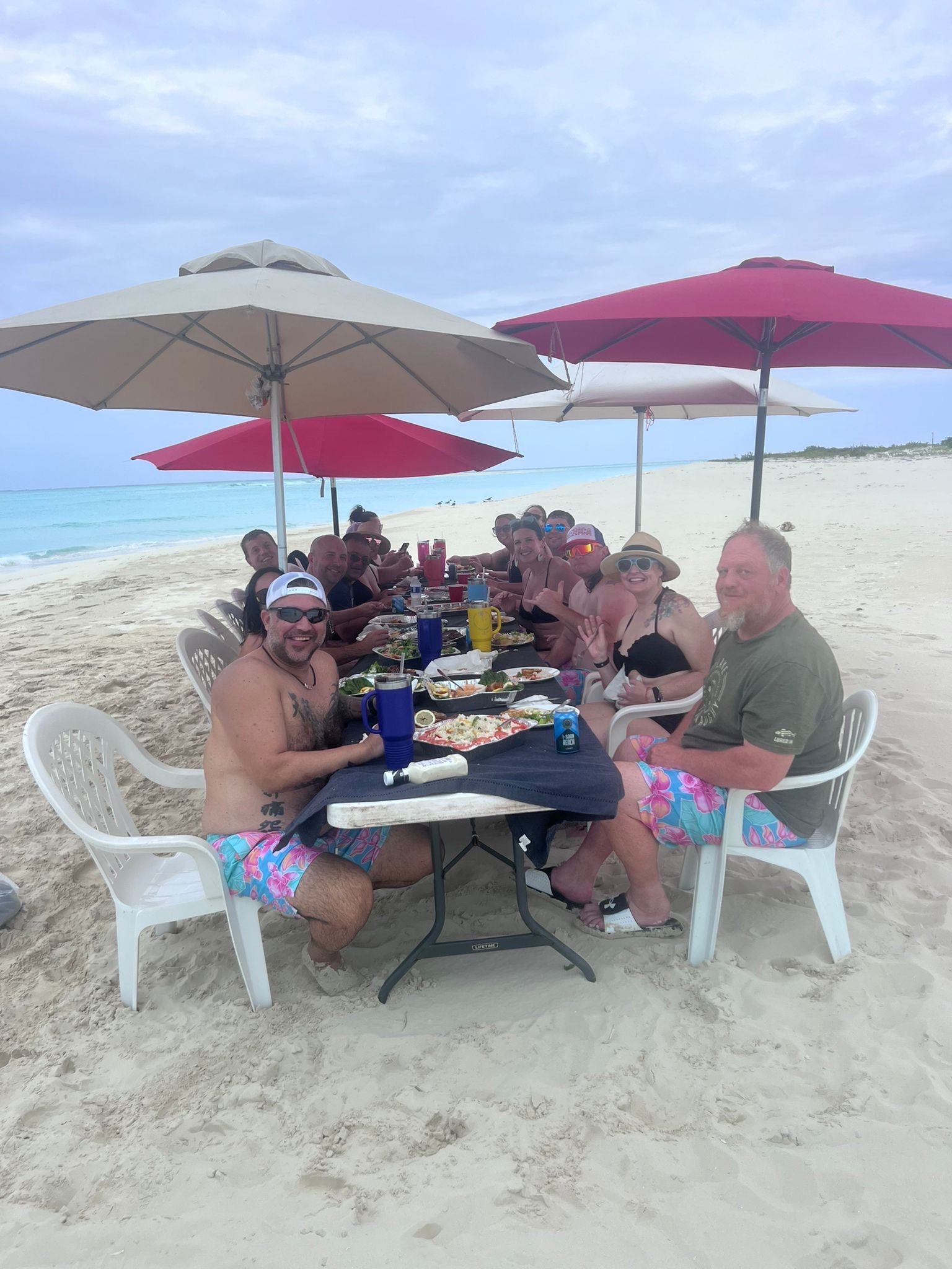 Kenard cruises yacht charter turks and caicos with Group of friends enjoying a meal on the beach, seated under umbrellas. The scene features food, drinks, and a coastal backdrop, capturing a festive atmosphere.