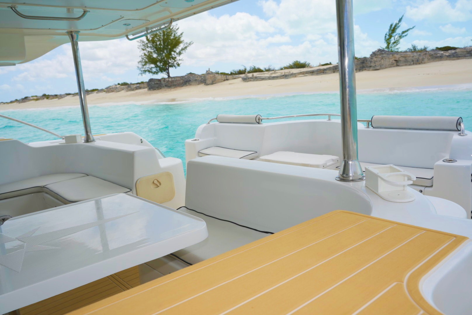 Luxurious catamaran seating overlooks a serene turquoise sea and sandy beach, offering a relaxing spot to enjoy the coastal view.